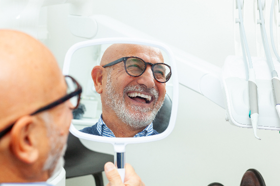man smiling in the mirror, showing his new dental implants