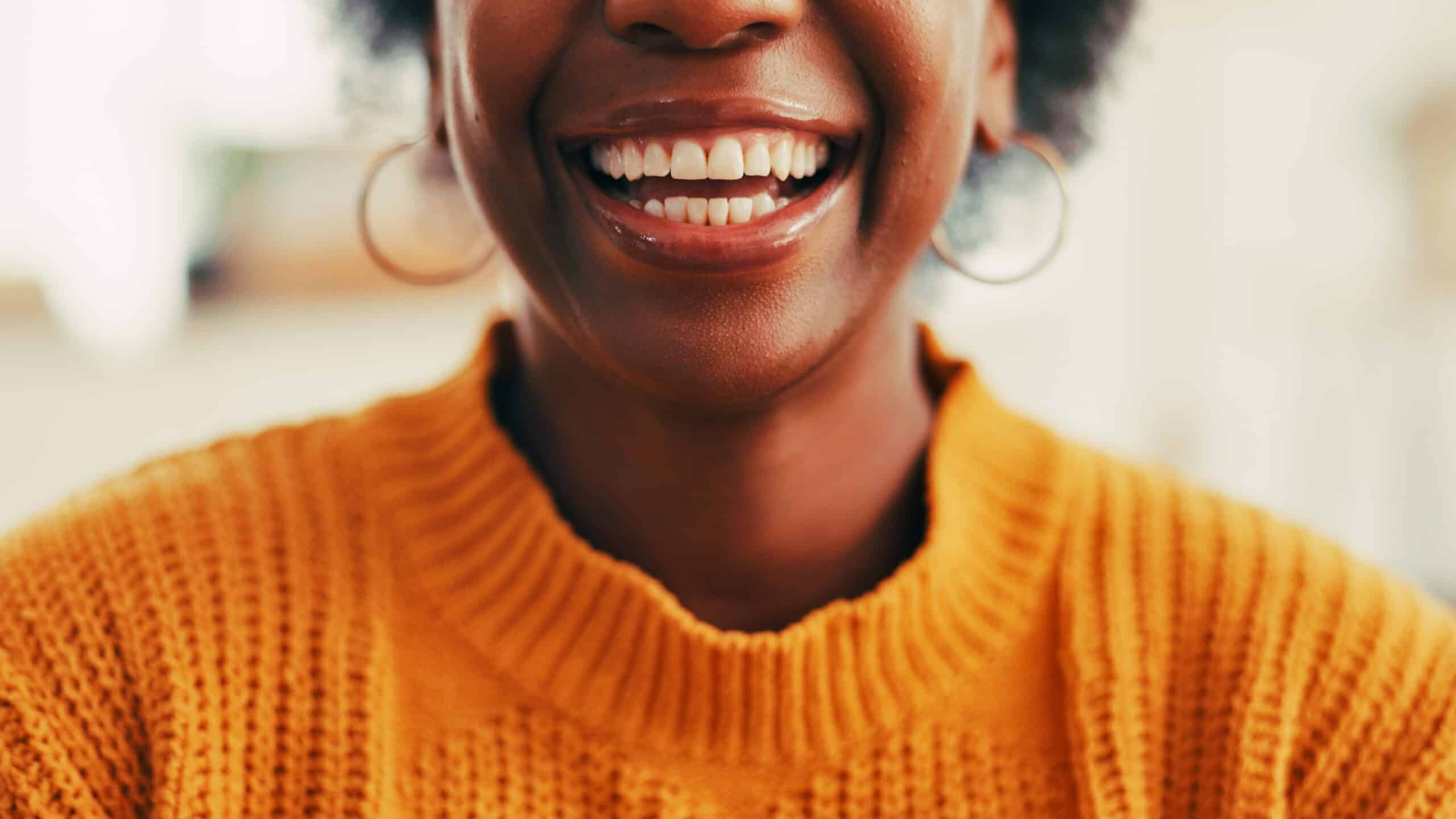 closeup of a woman in an orange sweater showing perfect smile