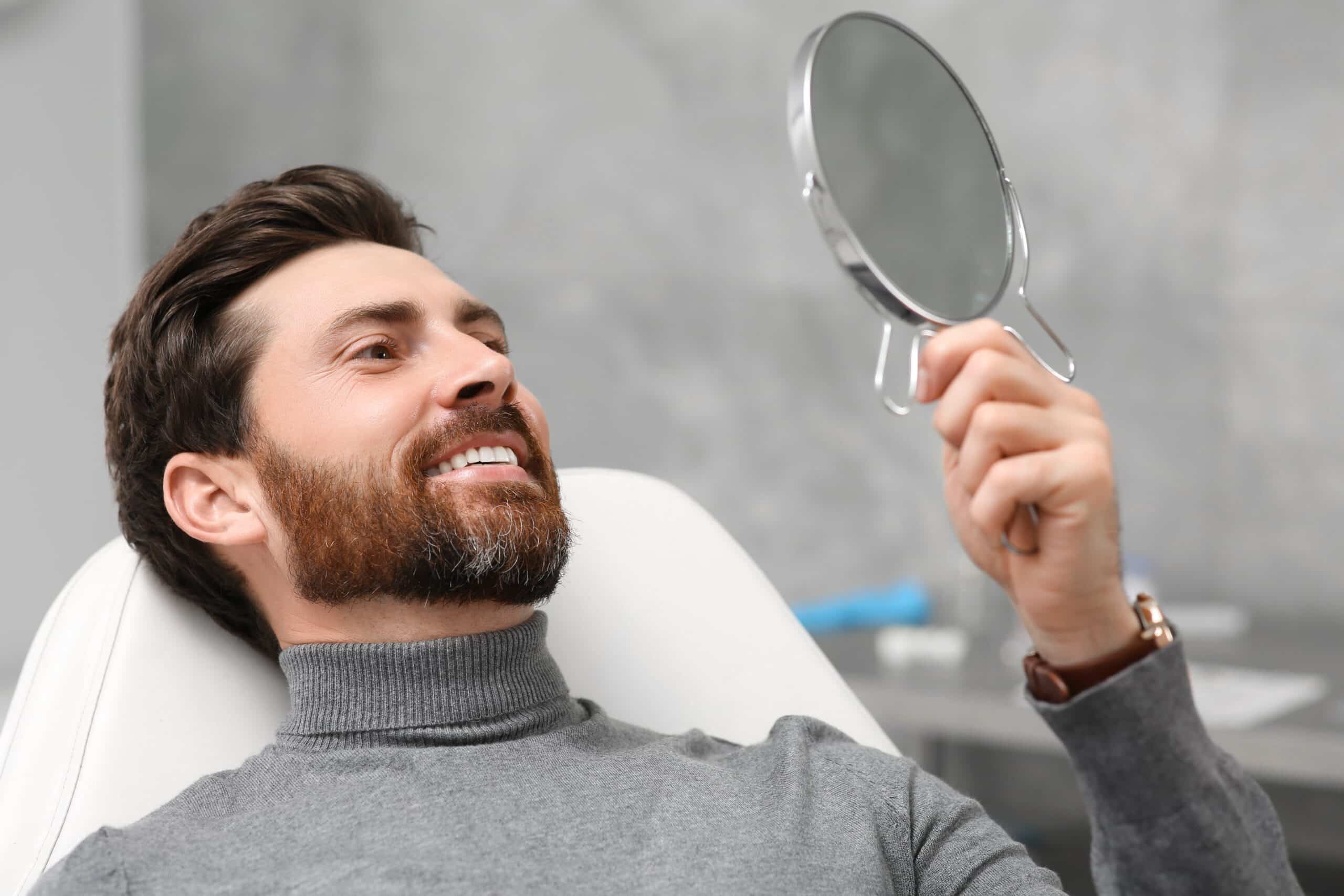 smiling man looking at his new dental implants in a mirror